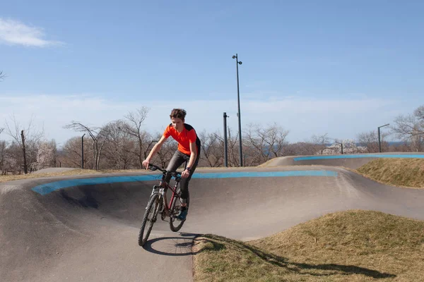 A teenager rides a bicycle on a pump track in a spring park, a guy goes in for sports