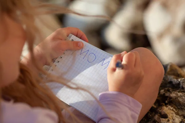 Kinderhand Schreibt Das Wort Mama Ein Notizbuch Ein Mädchen Sitzt — Stockfoto