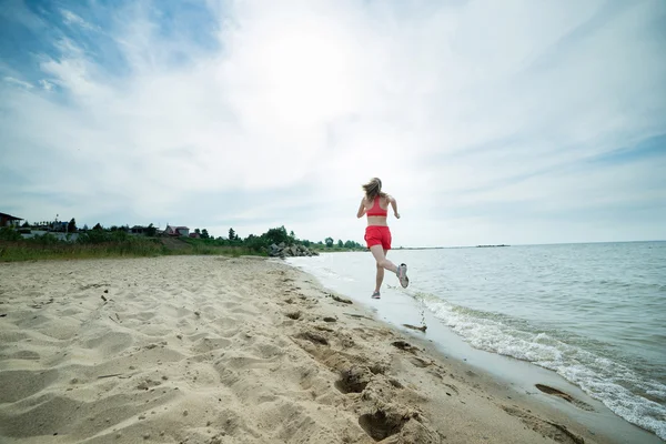 年轻的女士在阳光灿烂的夏天砂沙滩上运行。锻炼。慢跑 — 图库照片