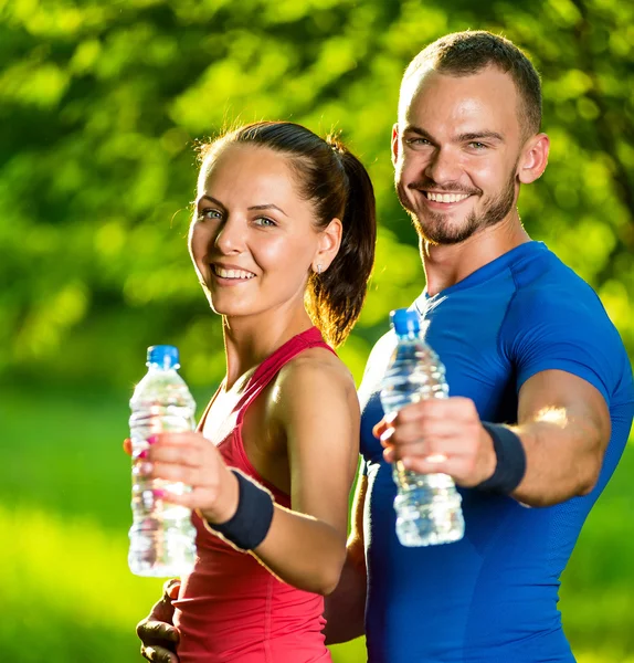 Uomo e donna che bevono acqua dalla bottiglia dopo l'esercizio fisico — Foto Stock