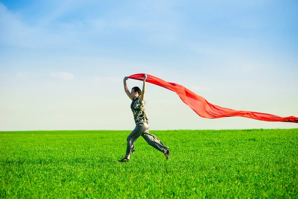 Beautiful young woman jumping on a green meadow with colored tissue — Stock Photo, Image