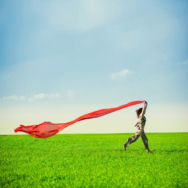 Mulher bonita pulando em um prado verde com tecido colorido — Fotografia de Stock