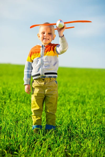 Happy boy playing with toy airplane against blue summer sky and green field background. — Stock Photo, Image