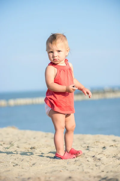 Mädchen im roten Kleid spielt am Sandstrand am Meer. — Stockfoto