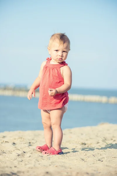 Mädchen im roten Kleid spielt am Sandstrand am Meer. — Stockfoto