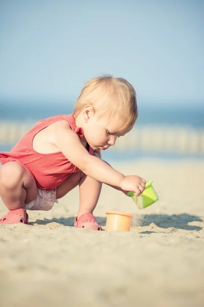 Bambina in abito rosso che gioca sulla spiaggia di sabbia vicino al mare . — Foto Stock