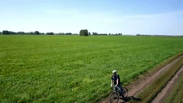 Antenne: Junger Mann radelt auf Landstraße durch grünes und gelbes Feld. — Stockvideo