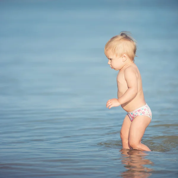 Schattige baby spelen op het zandstrand en in zeewater. — Stockfoto