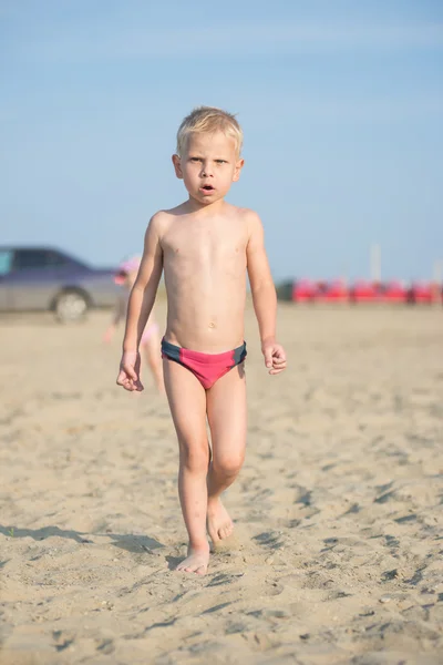 Ładny chłopczyk chodzenie na piaszczystej plaży w pobliżu morza. Na wybrzeżu Oceanu. — Zdjęcie stockowe