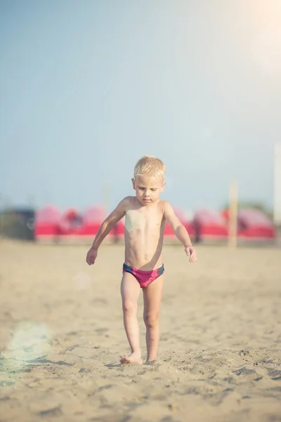 Ładny chłopczyk chodzenie na piaszczystej plaży w pobliżu morza. Na wybrzeżu Oceanu. — Zdjęcie stockowe