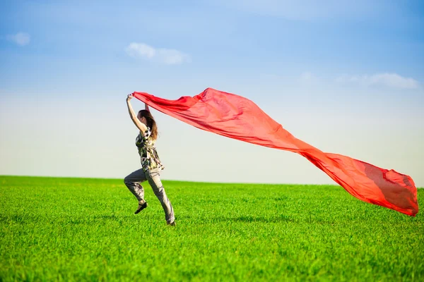 Belle jeune femme sautant sur une prairie verte avec des tissus colorés — Photo