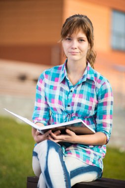 Öğrenci kızla defterini bankta. Yaz kampüs park.