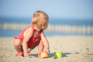 Denize yakın kumlu plajda oynayan Kırmızı elbiseli kız bebek.