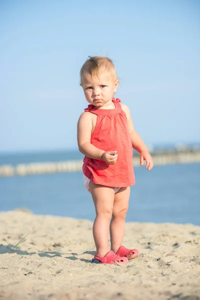 Mädchen im roten Kleid spielt am Sandstrand am Meer. — Stockfoto