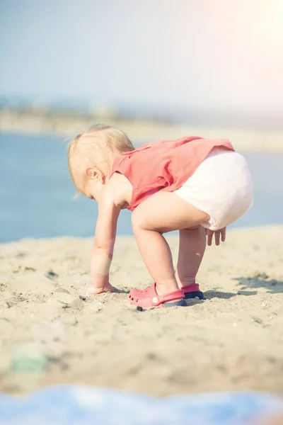 Niña en vestido rojo jugando en la playa de arena cerca del mar . —  Fotos de Stock