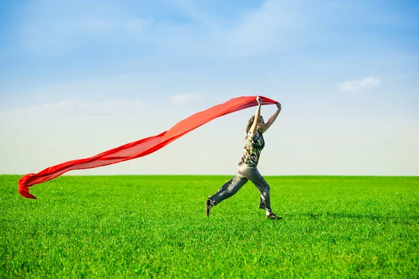 Beautiful young woman jumping on a green meadow with colored tissue — Stock Photo, Image