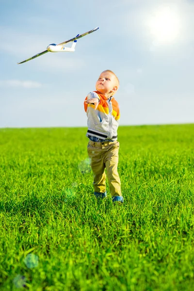 Niño feliz jugando con el avión de juguete contra el cielo azul de verano y el fondo verde del campo . — Foto de Stock