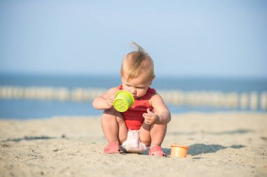 Denize yakın kumlu plajda oynayan Kırmızı elbiseli kız bebek.