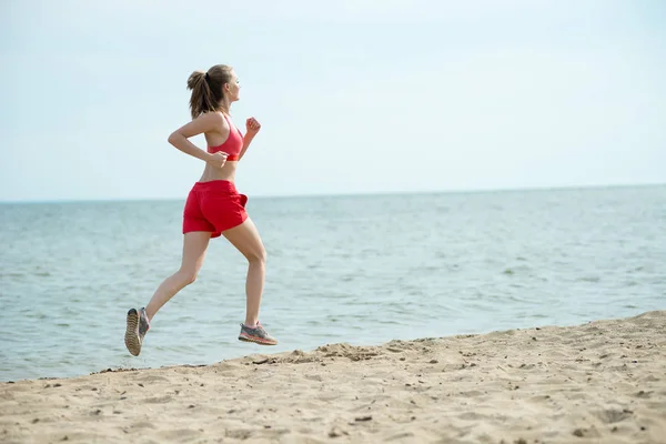 Giovane signora che corre alla soleggiata spiaggia di sabbia estiva. Allenati. Jogging — Foto Stock