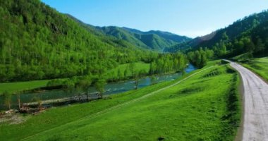 UHD 4k havadan görünümü. Düşük uçuş taze soğuk dağ nehir, çayır ve yola güneşli yaz sabahı.