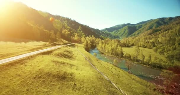 UHD 4K vista aérea. Vuelo bajo sobre el río fresco y frío de la montaña, prado y carretera en la soleada mañana de verano . — Vídeo de stock