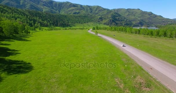 汽车在一条蜿蜒的小路在山和草甸上空飞行。农村公路下面. — 图库视频影像