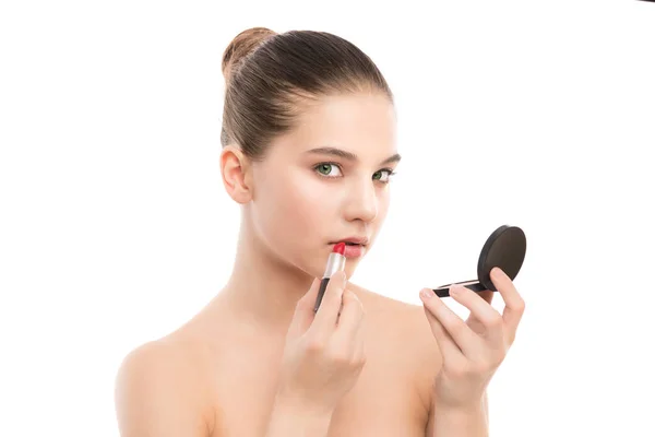 Giovane donna bruna con viso pulito perfetto applicare il rossetto usando lo specchio. Isolato su un bianco . — Foto Stock