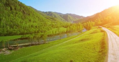 UHD 4k havadan görünümü. Düşük uçuş taze soğuk dağ nehir, çayır ve yola güneşli yaz sabahı.