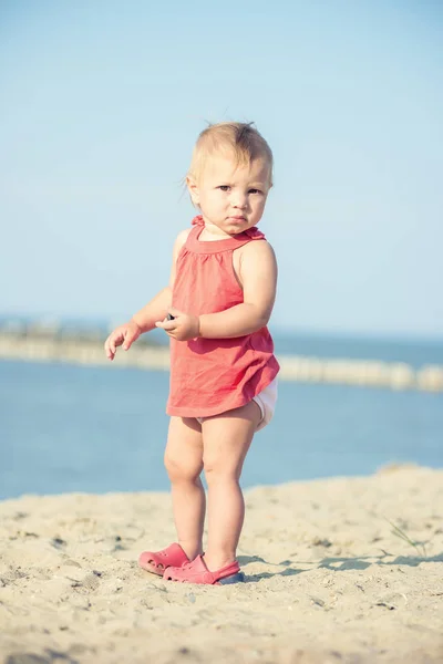 Mädchen im roten Kleid spielt am Sandstrand am Meer. — Stockfoto