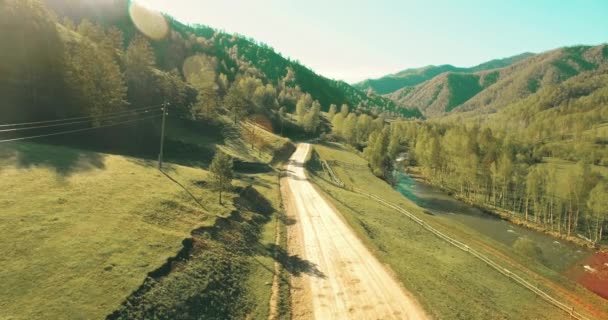 Vista aérea UHD 4K. Vôo de ar baixo sobre montanha estrada de terra rural e prado na manhã de verão ensolarada — Vídeo de Stock