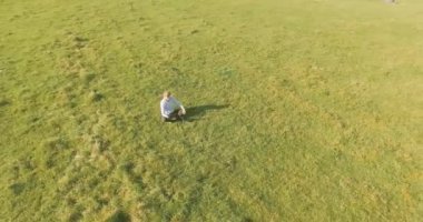 UHD 4k havadan görünümü. Defter pad ile yeşil çim sahasında oturan işadamı üzerinde düşük yörünge uçuş