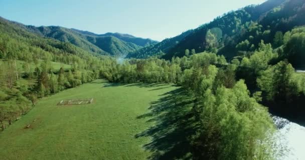 Voo no meio do ar sobre o rio e o prado da montanha fresca na ensolarada manhã de verão. Estrada de terra rural abaixo . — Vídeo de Stock