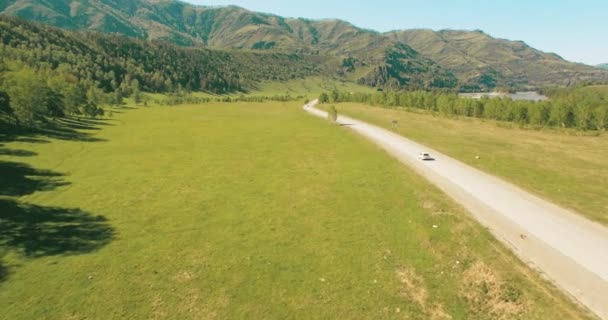 Vuelo sobre los coches en un camino sinuoso en las colinas y el prado. Carretera rural abajo . — Vídeo de stock