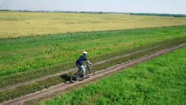 AERIAL: Joven ciclista en bicicleta en camino rural por campo verde y amarillo . — Vídeos de Stock