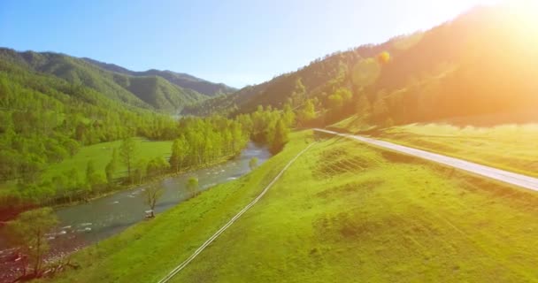 UHD 4k luchtfoto. Lage vlucht over verse koude berg rivier, weide en weg bij zonnige Zomerochtend. — Stockvideo