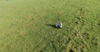 UHD 4k havadan görünümü. Defter pad ile yeşil çim sahasında oturan işadamı üzerinde düşük yörünge uçuş