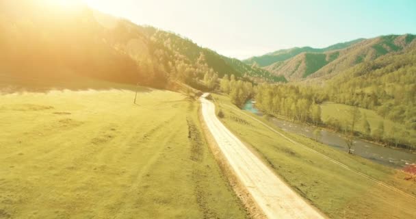 Vista aérea UHD 4K. Vuelo de aire bajo sobre carretera de tierra rural de montaña y prado en la soleada mañana de verano . — Vídeos de Stock