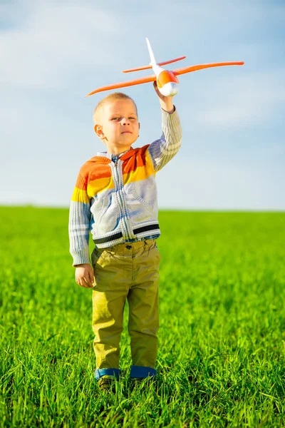 Gelukkige jongen spelen met speelgoed vliegtuig tegen blauwe zomer hemel en groen veld achtergrond. — Stockfoto