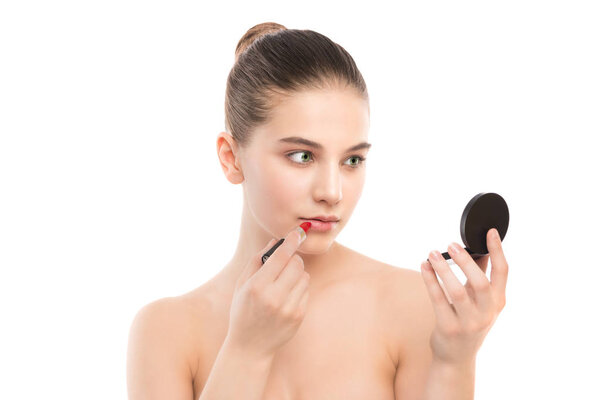 Young brunette woman with perfect clean face applying lipstick using mirror. Isolated on a white.