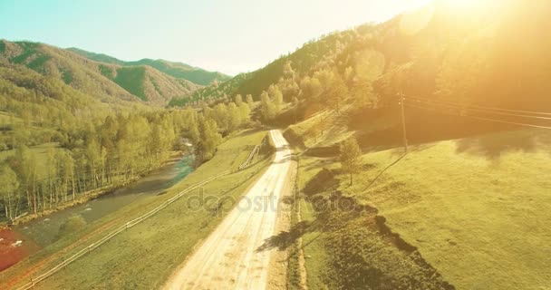 Vista aérea UHD 4K. Vôo de ar baixo sobre montanha estrada de terra rural e prado na manhã de verão ensolarada . — Vídeo de Stock