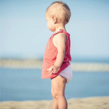 Denize yakın kumlu plajda oynayan Kırmızı elbiseli kız bebek.