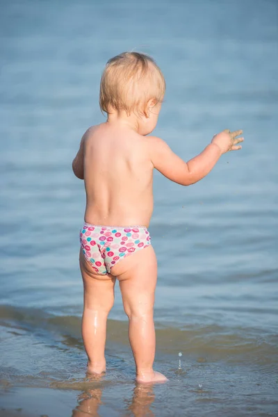 Bebê bonito brincando na praia e na água do mar . — Fotografia de Stock