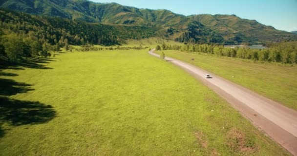 Vuelo sobre los coches en un camino sinuoso en las colinas y el prado. Carretera rural abajo . — Vídeos de Stock