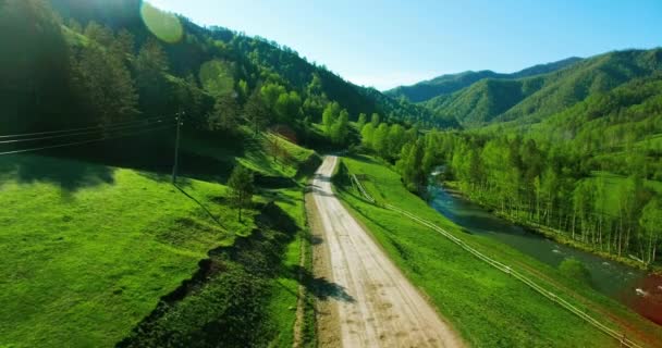 Vista aérea UHD 4K. Vuelo de aire bajo sobre carretera de tierra rural de montaña y prado en la soleada mañana de verano . — Vídeo de stock