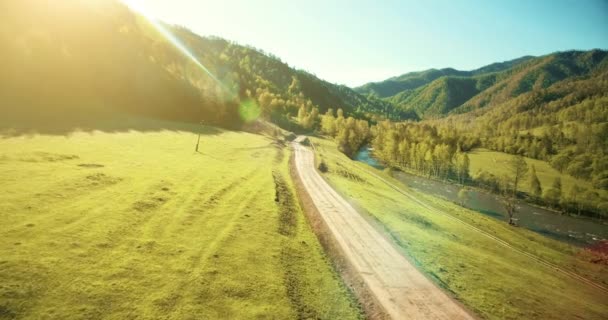 Vista aérea UHD 4K. Vôo de ar baixo sobre montanha estrada de terra rural e prado na manhã de verão ensolarada . — Vídeo de Stock