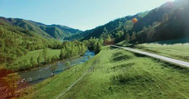 UHD 4k havadan görünümü. Düşük uçuş taze soğuk dağ nehir, çayır ve yola güneşli yaz sabahı.