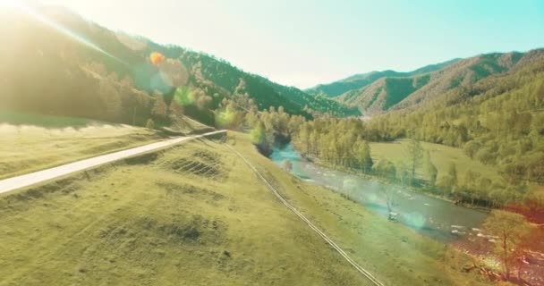 UHD 4K vista aérea. Vuelo bajo sobre el río fresco y frío de la montaña, prado y carretera en la soleada mañana de verano . — Vídeos de Stock