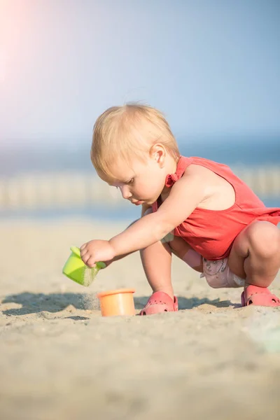Девочка в красном платье играет на песчаном пляже у моря . — стоковое фото