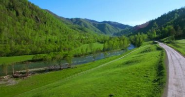 UHD 4k havadan görünümü. Düşük uçuş taze soğuk dağ nehir, çayır ve yola güneşli yaz sabahı.