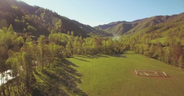 Mid air flight over fresh mountain river and meadow at sunny summer morning. Rural dirt road below. — Stock Video